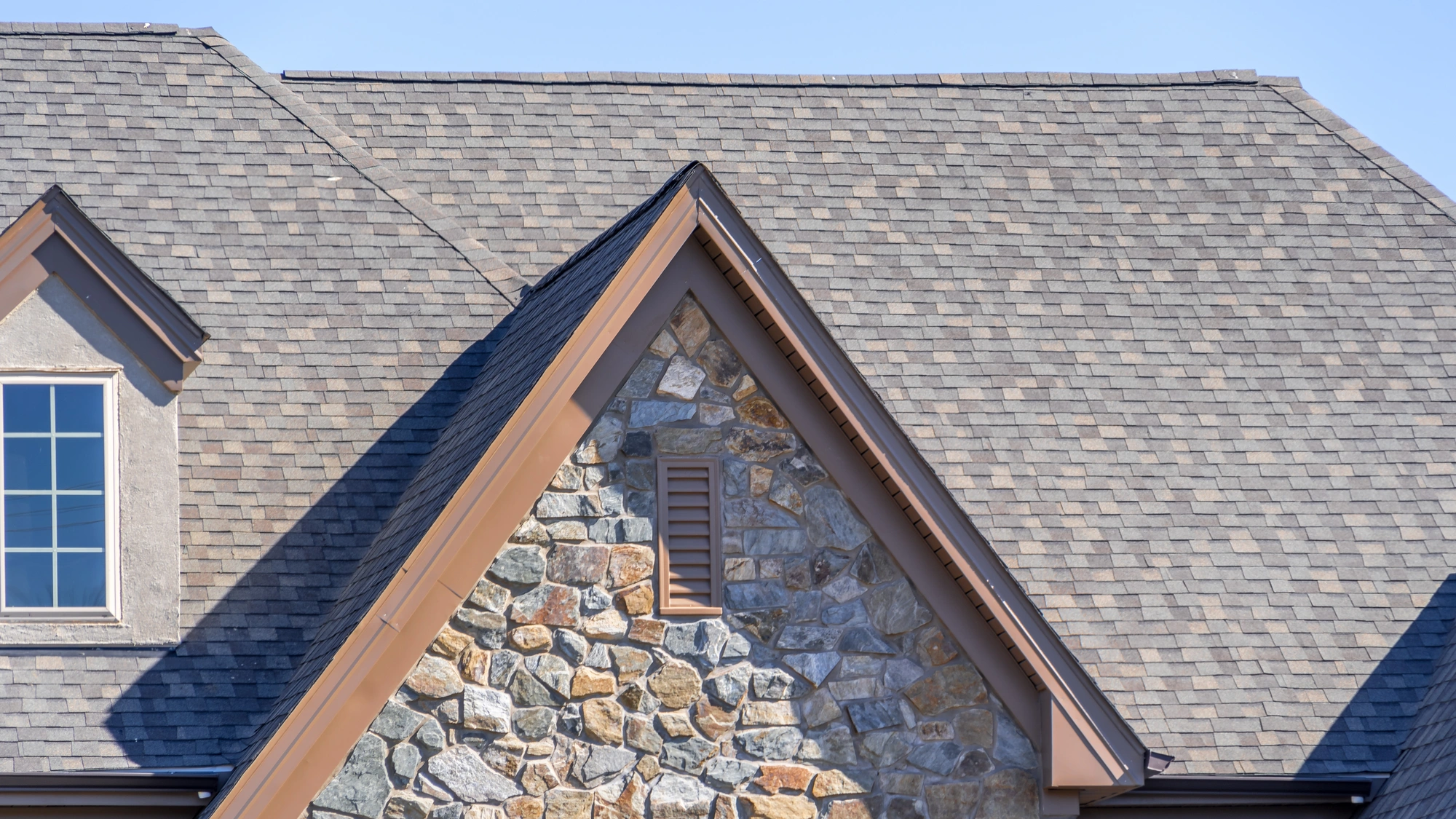 A home with stone siding and a gray shingle roof