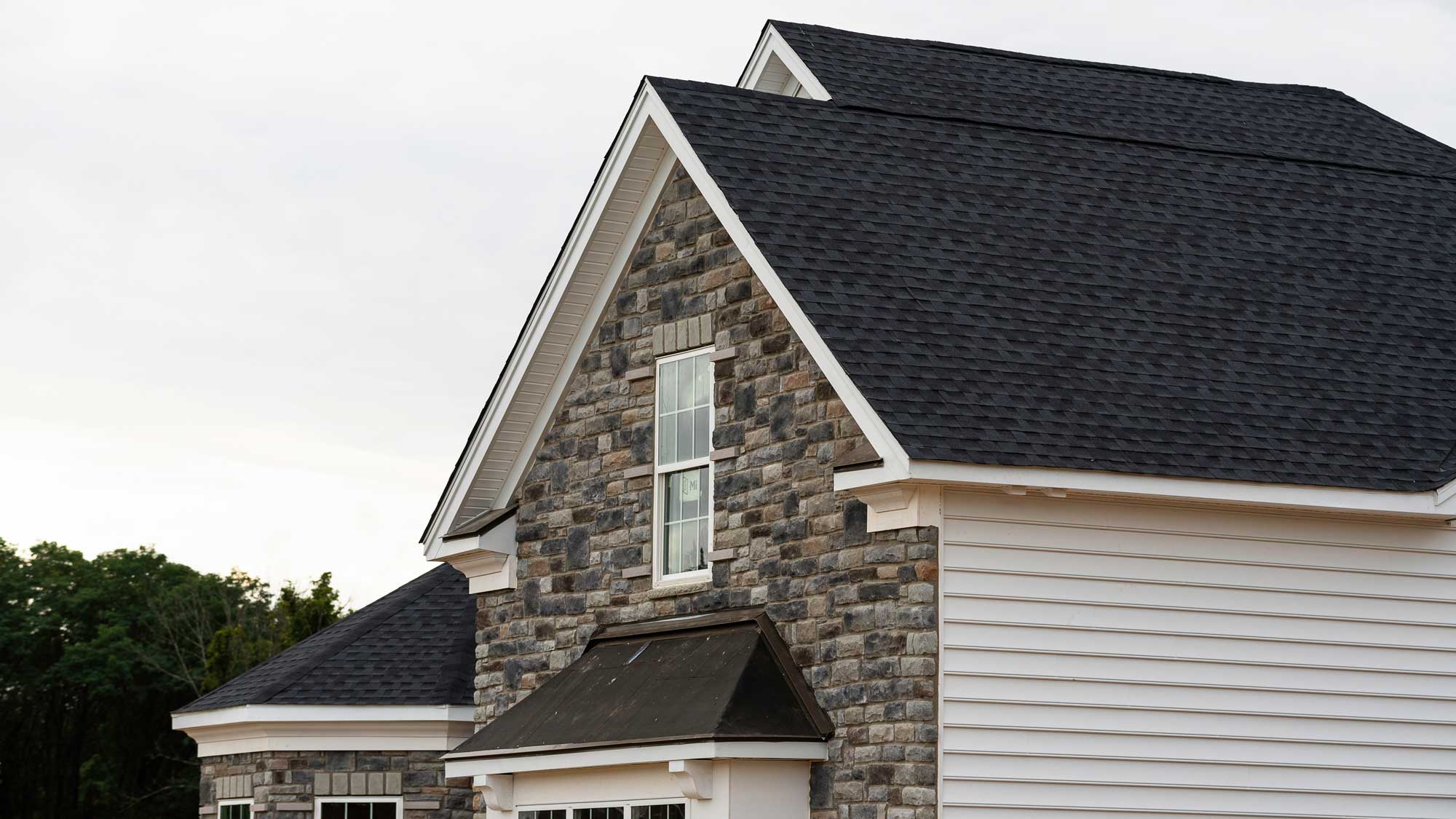 Closeup of a black shingle roof on a home with stone and white siding