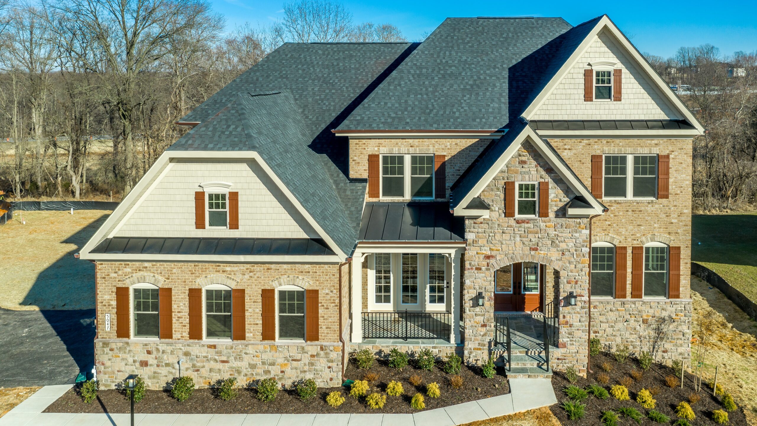 A large home with stone siding and a gray shingle roof