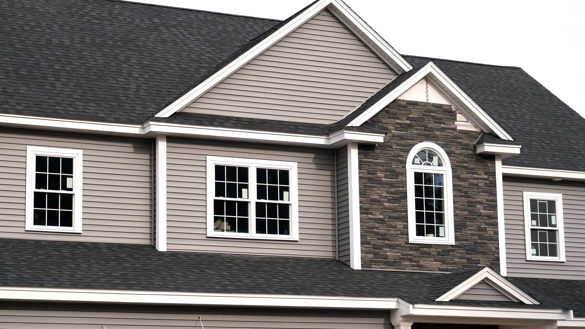 A tan-sided home with gray shingle roofing and newly installed windows