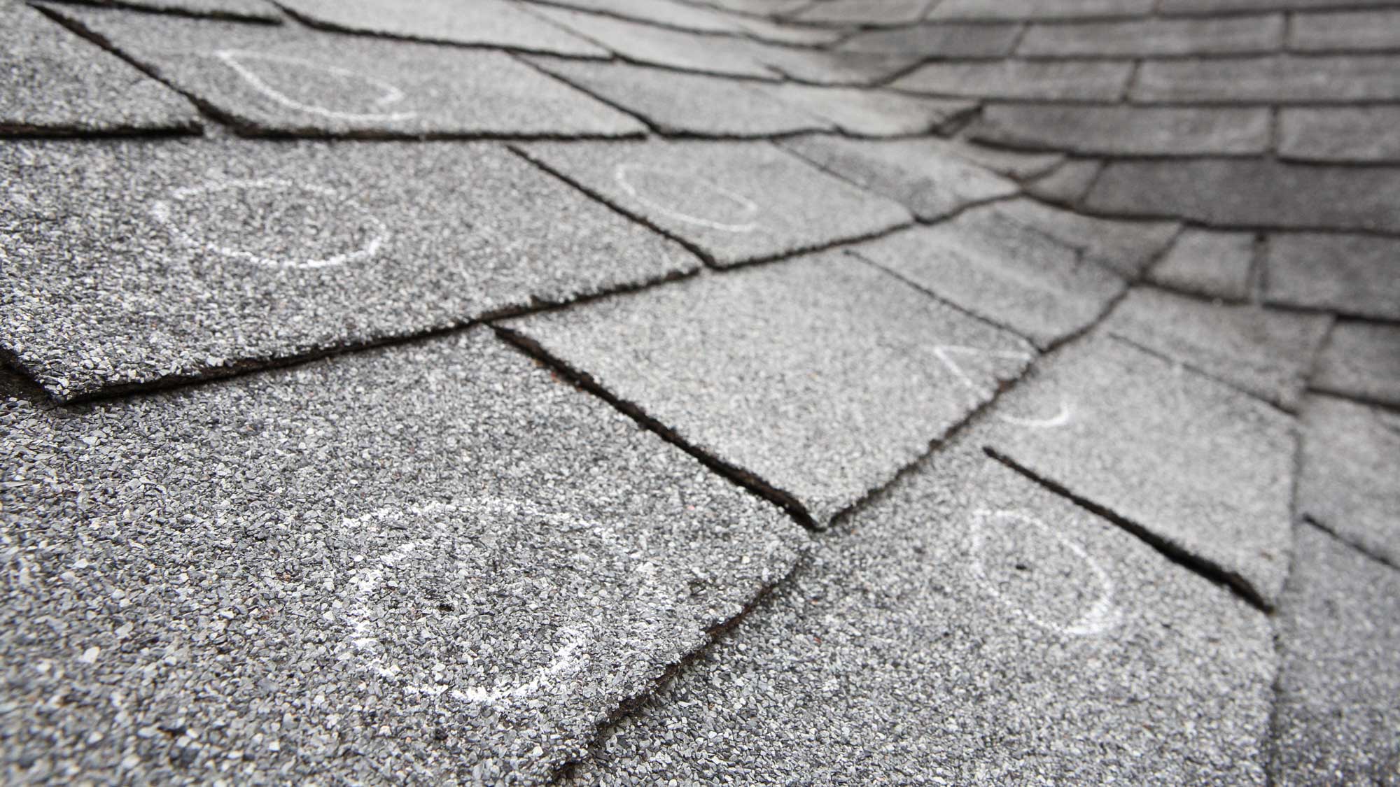 A shingle roof with damaged spots marked in chalk