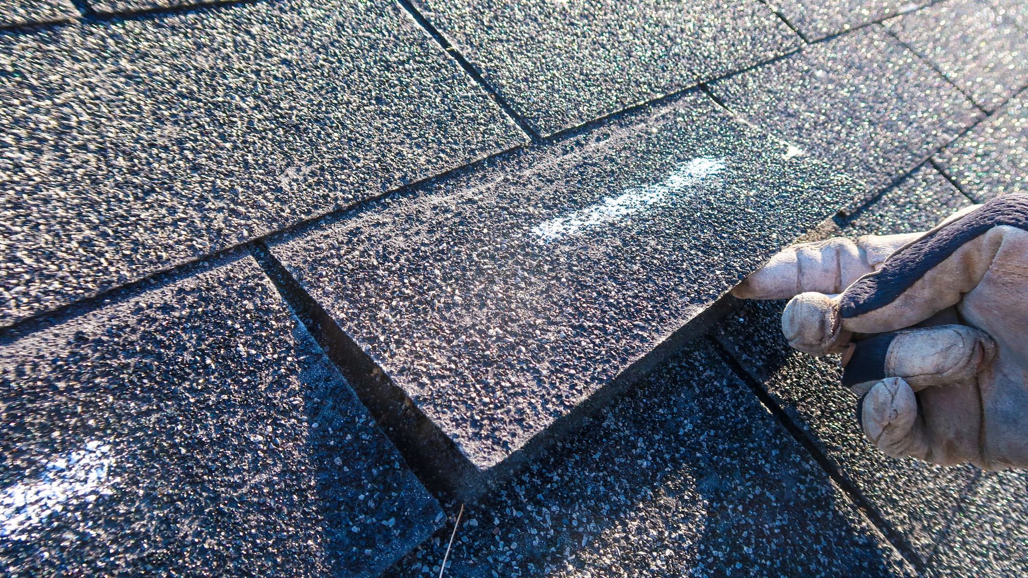 A roofing contractor completes an inspection, looking at a damaged shingle