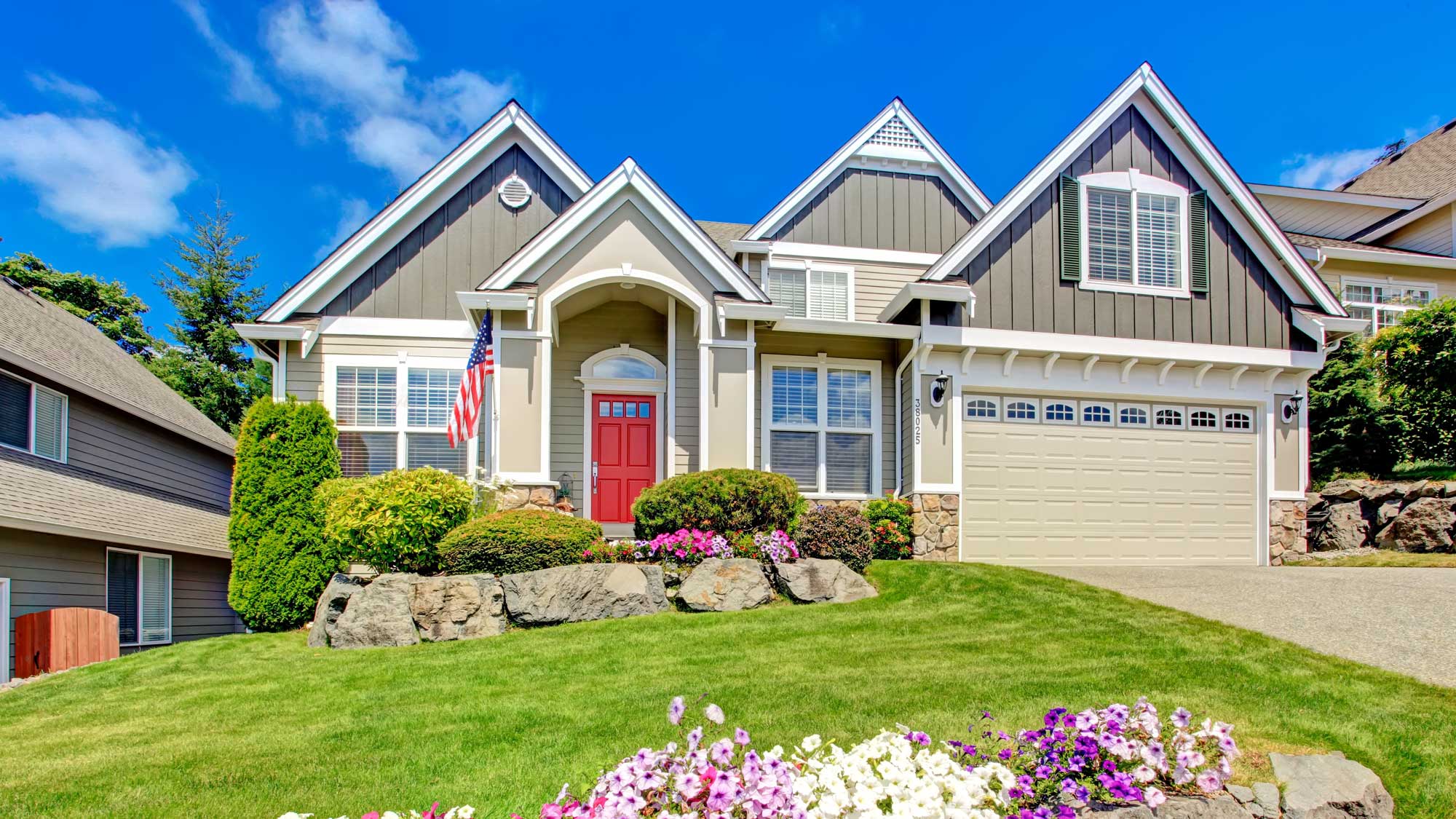 A large tan-sided home with white trim, a red door, and gray shingle roofing