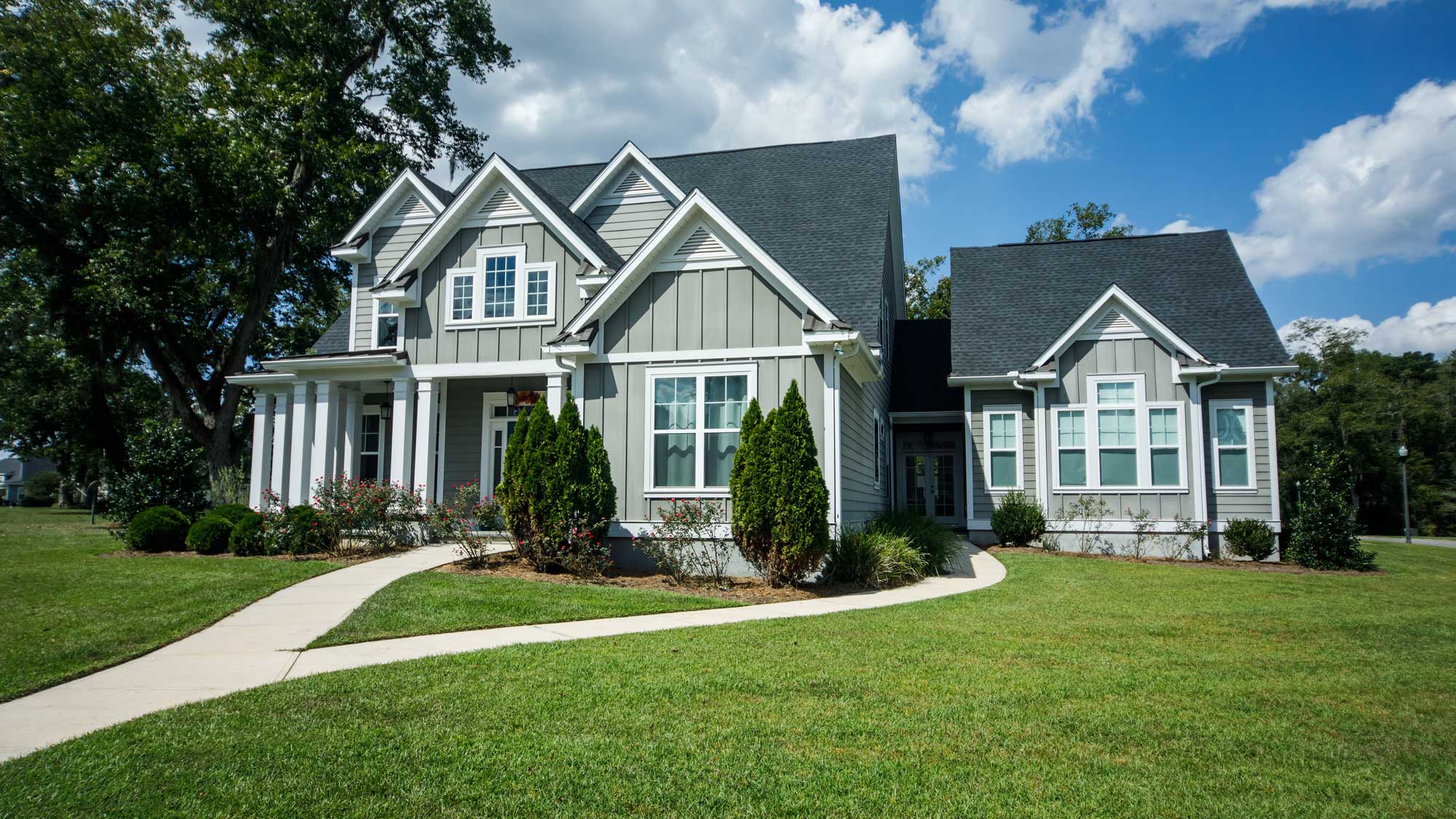 A large green-sided home with white trim and gray shingle roofing