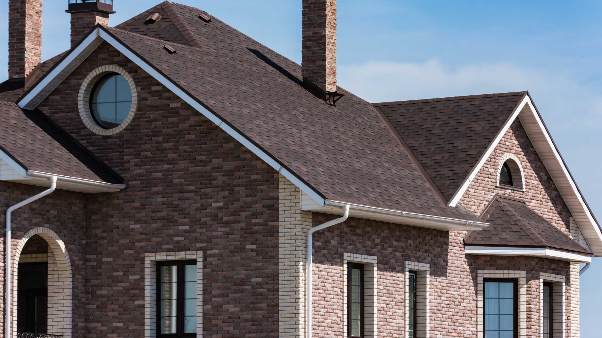 A brick home with a brown shingle roof