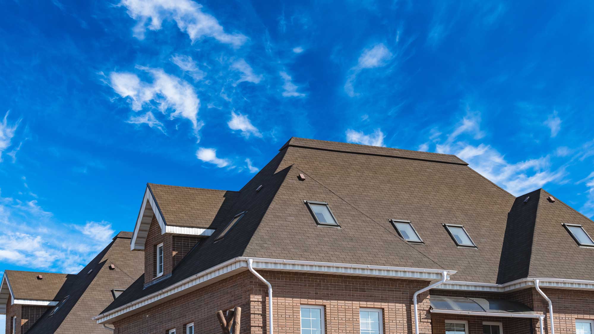 A brick home with a brown shingle roof, a dormer, and four skylights