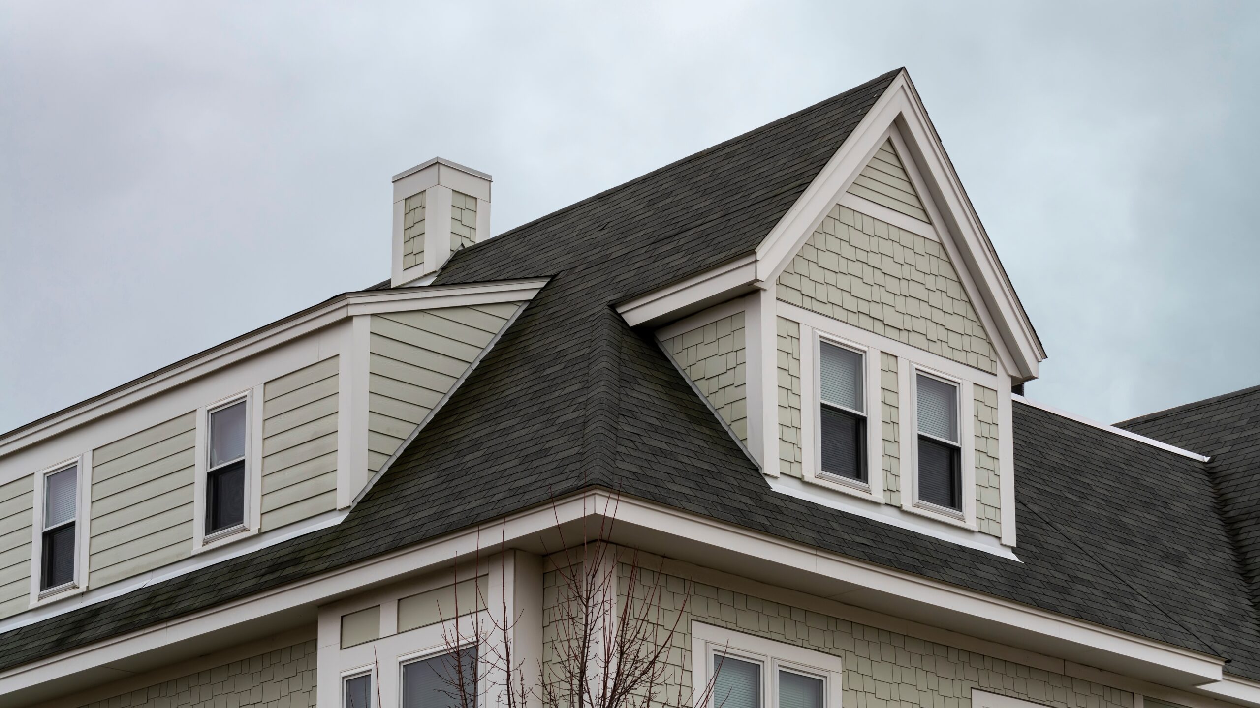 A two-story tan-sided home with white trim and a gray shingle roof