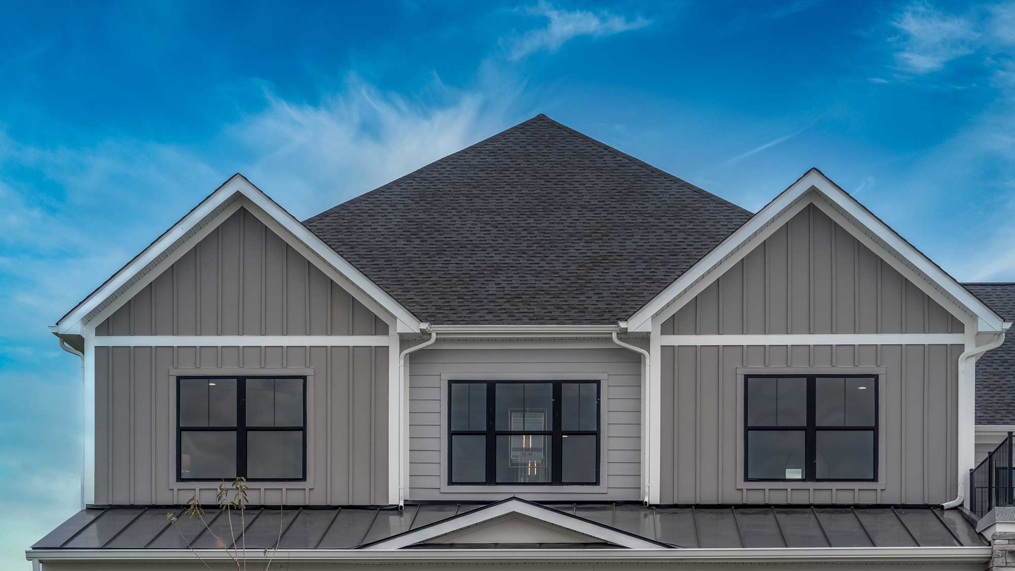 Closeup of the second story of a home with gray and white siding and a gray shingle roof