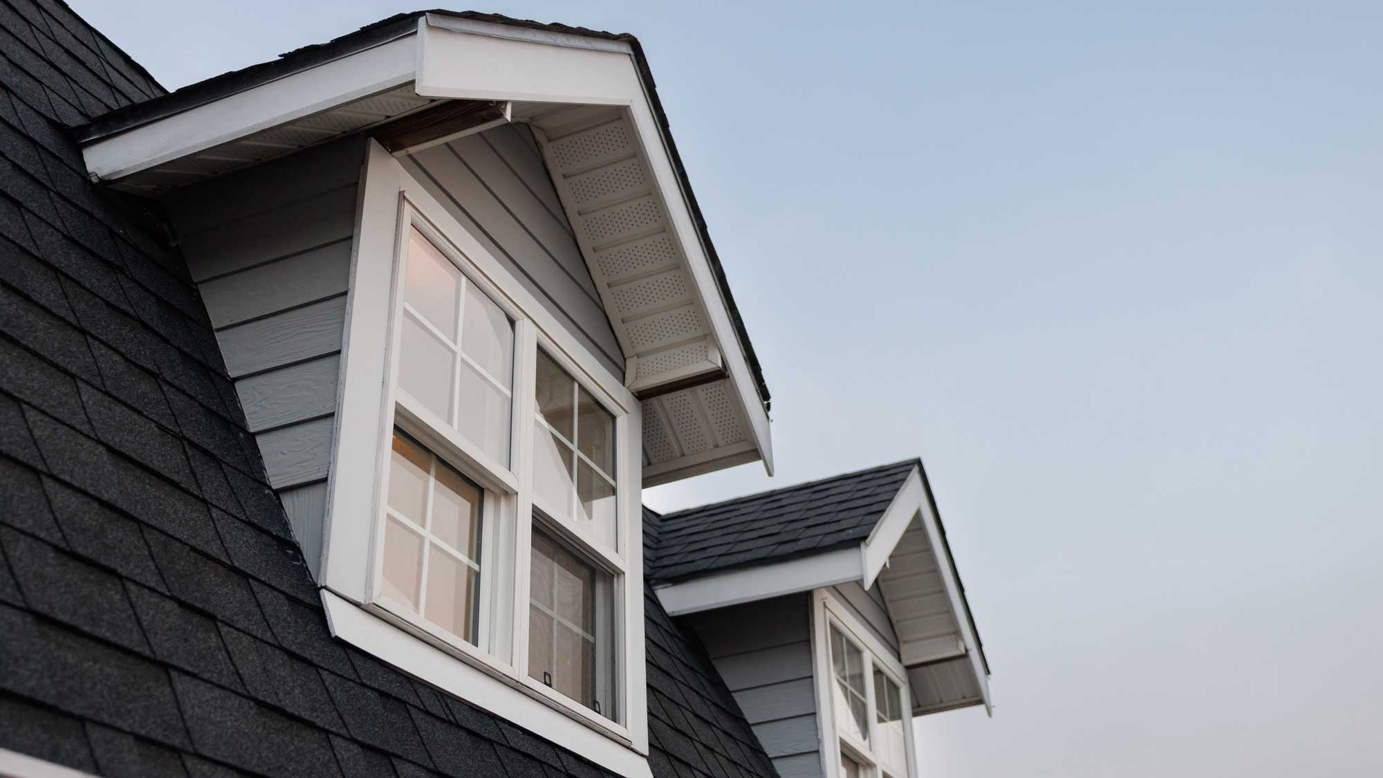 Closeup of a black shingle roof with two dormer windows