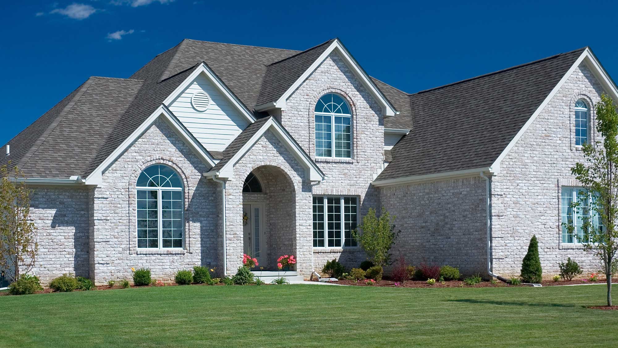 A large brick home with custom windows and a gray shingle roof