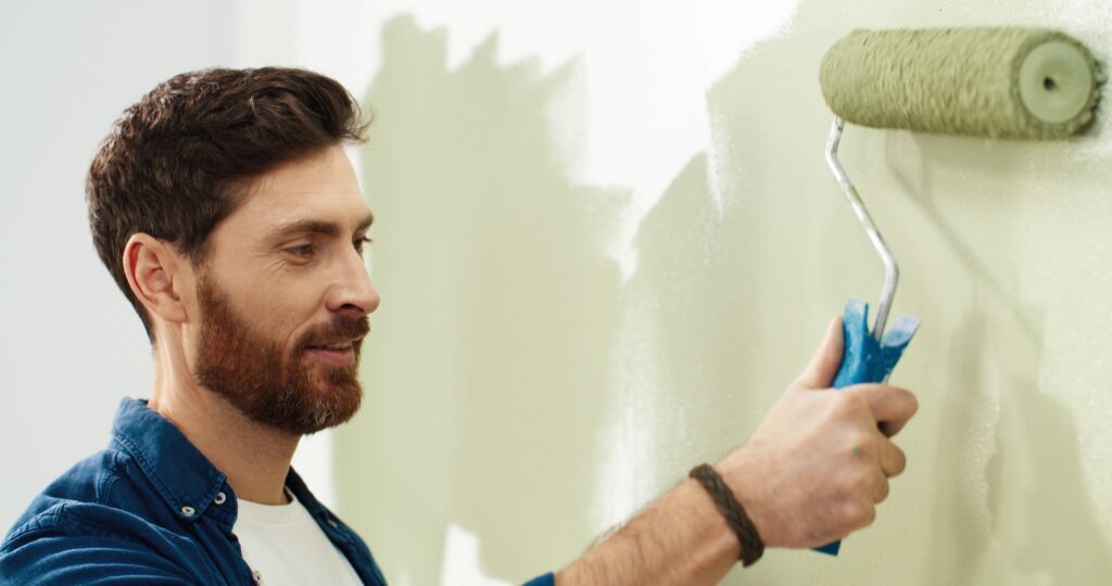 Man painting wall green with paint roller