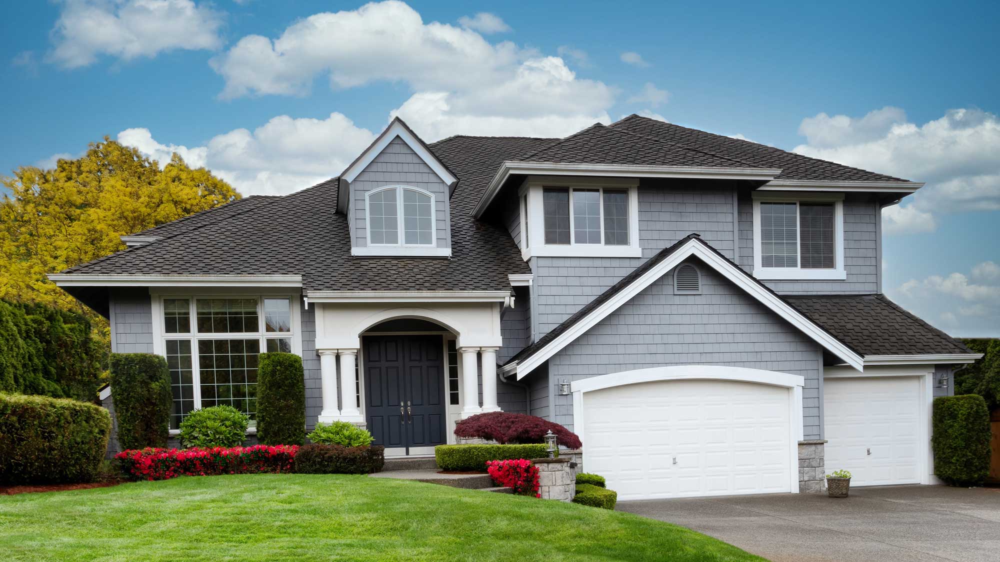 A large two-story home with blue-gray siding, white trim, and a gray asphalt shingle roof