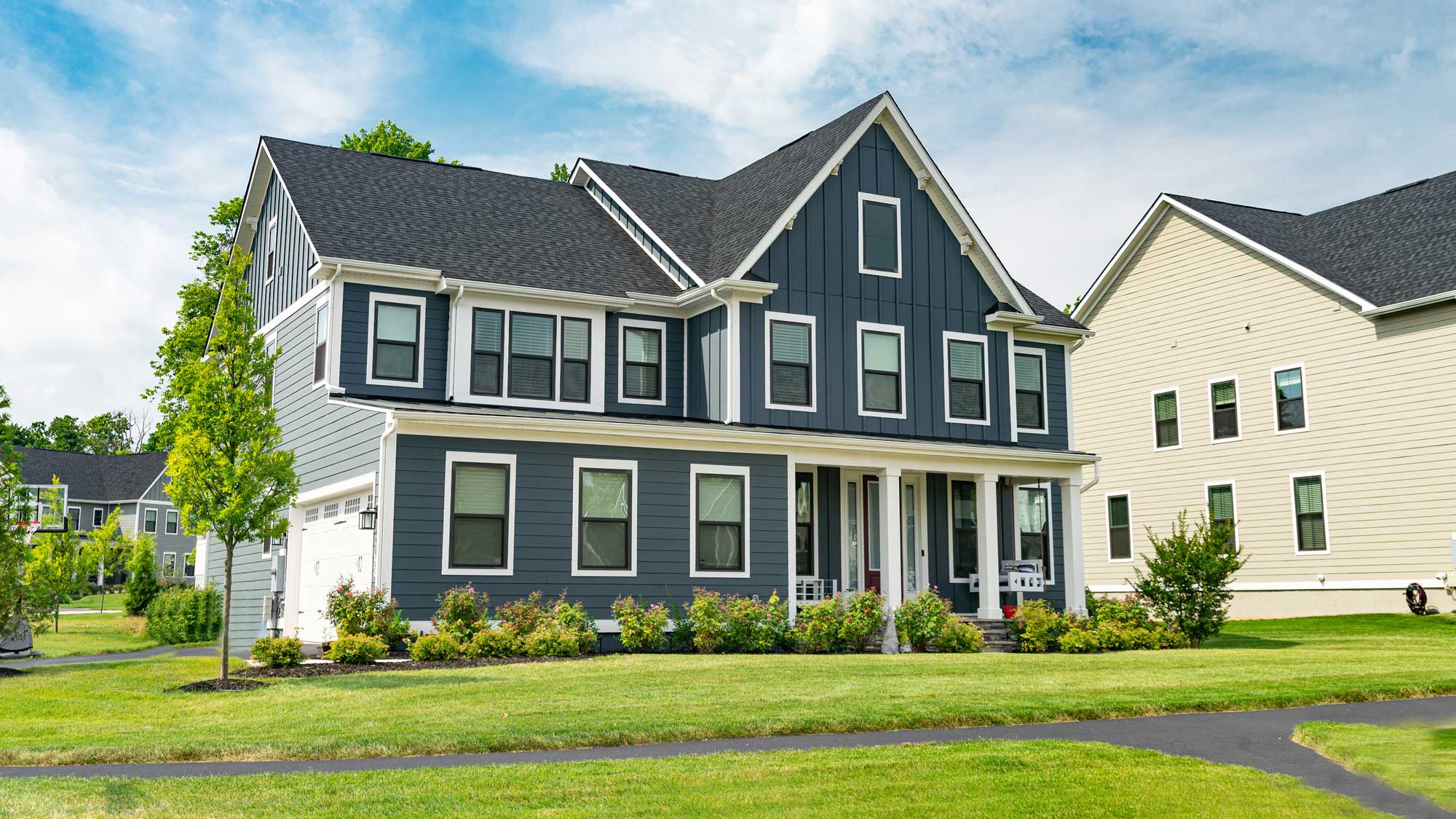 A large two-story home with blue siding, white trim, and a gray asphalt shingle roof