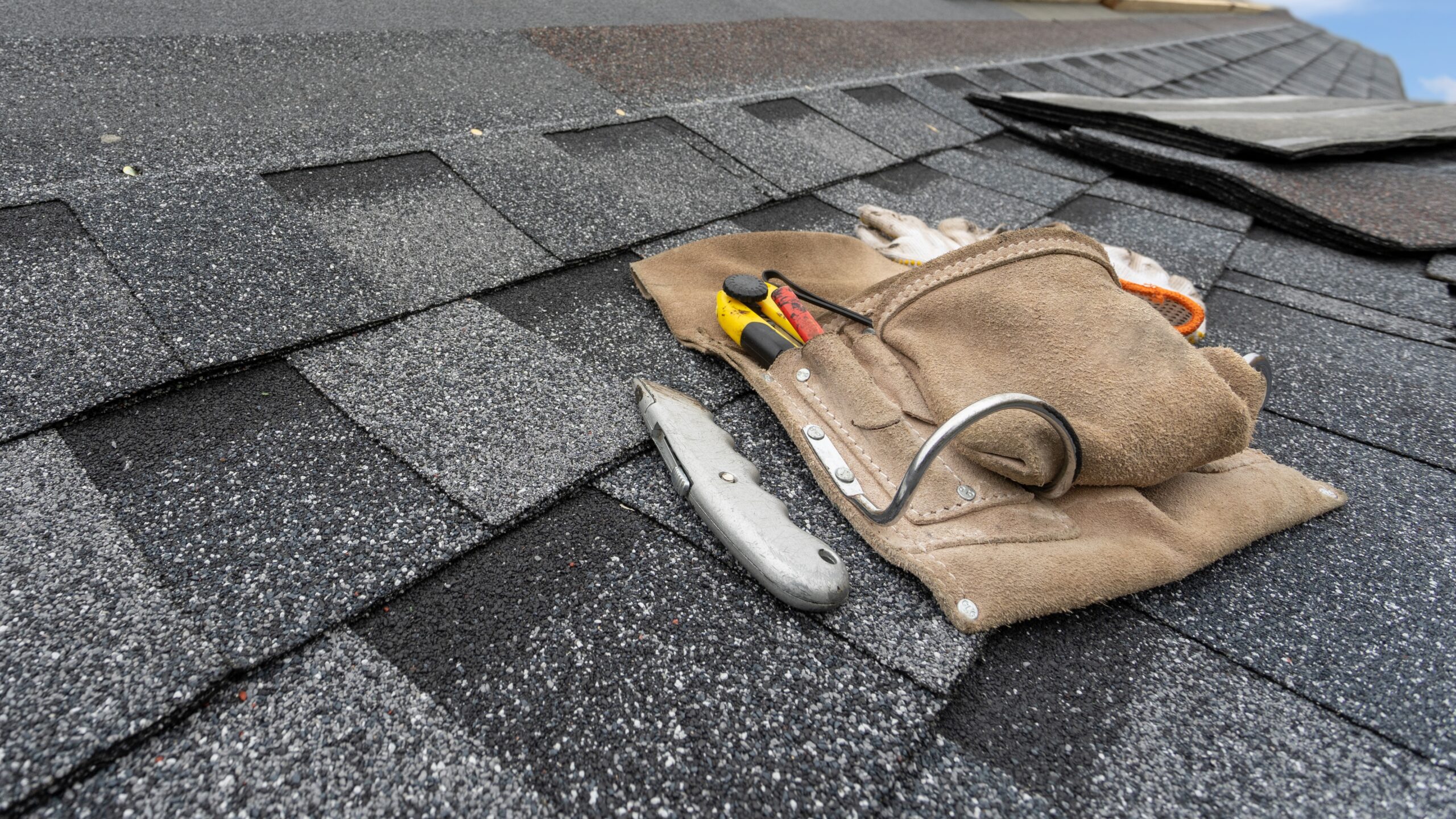 Closeup of toolbag and utility knife laying on a shingle roof