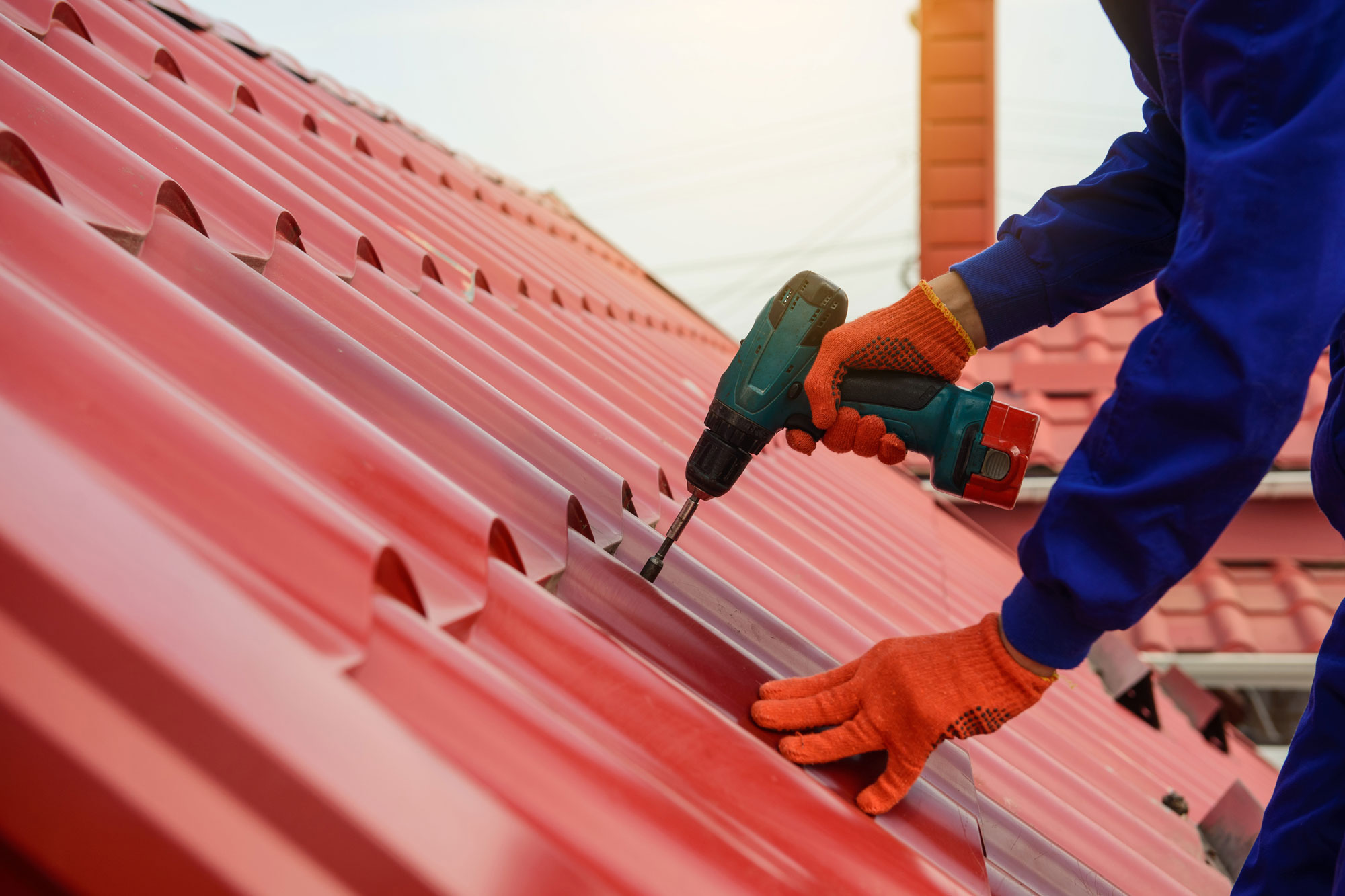 Roofer tightening screw on red metal roof