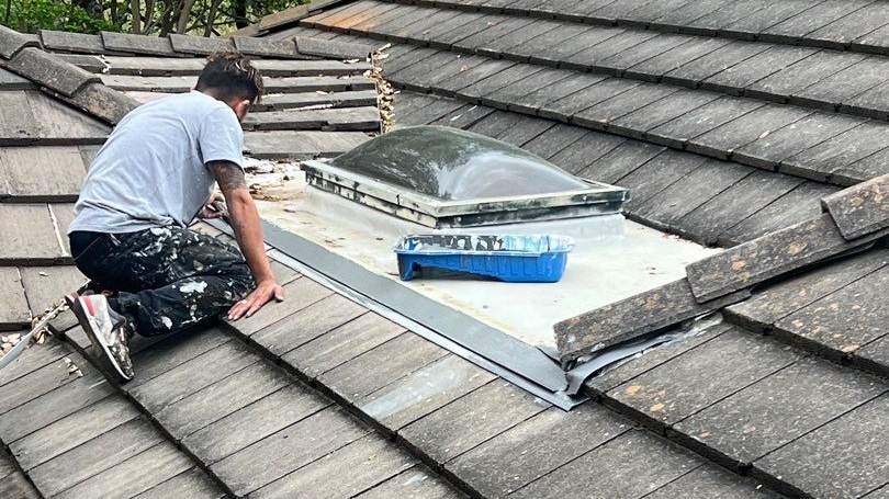 A roofer performs repairs on a roof with a skylight