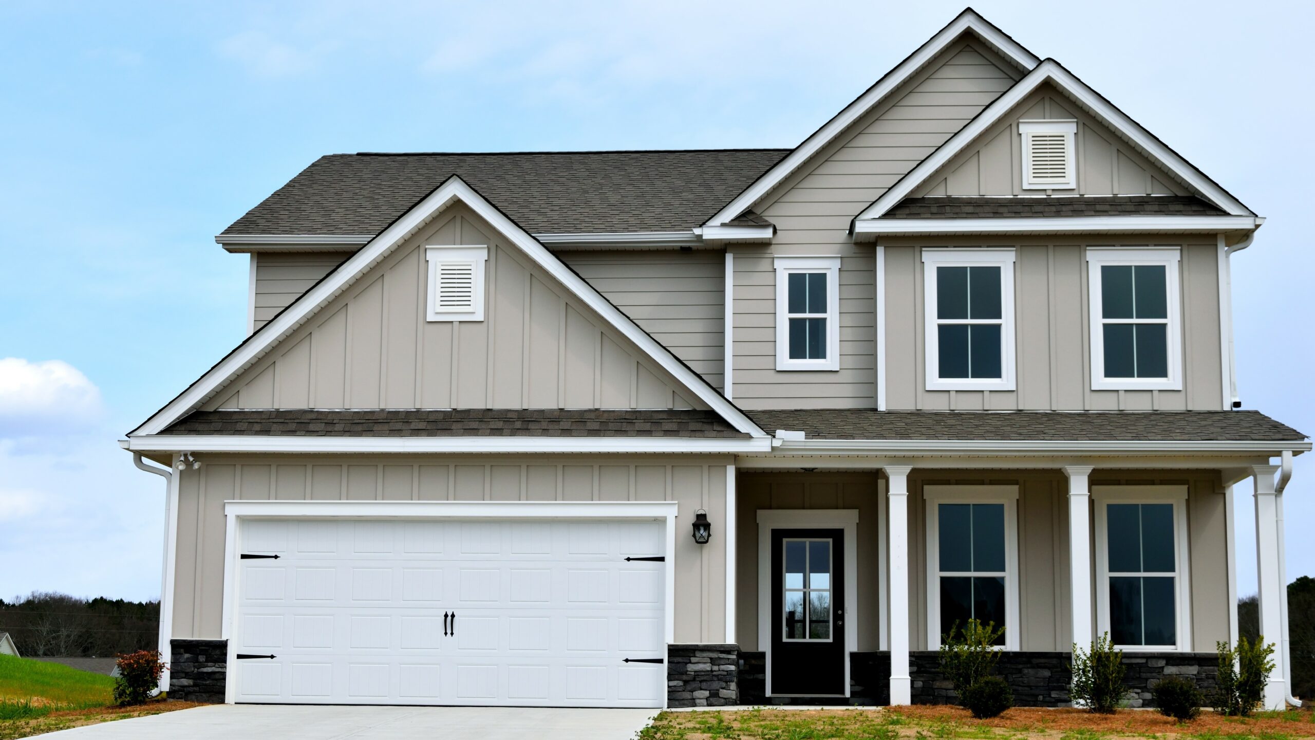 A tan-sided home with white trim and a gray shingle roof