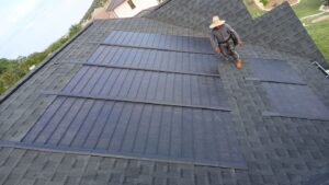 A roofer walking on an asphalt shingle and solar shingle roof