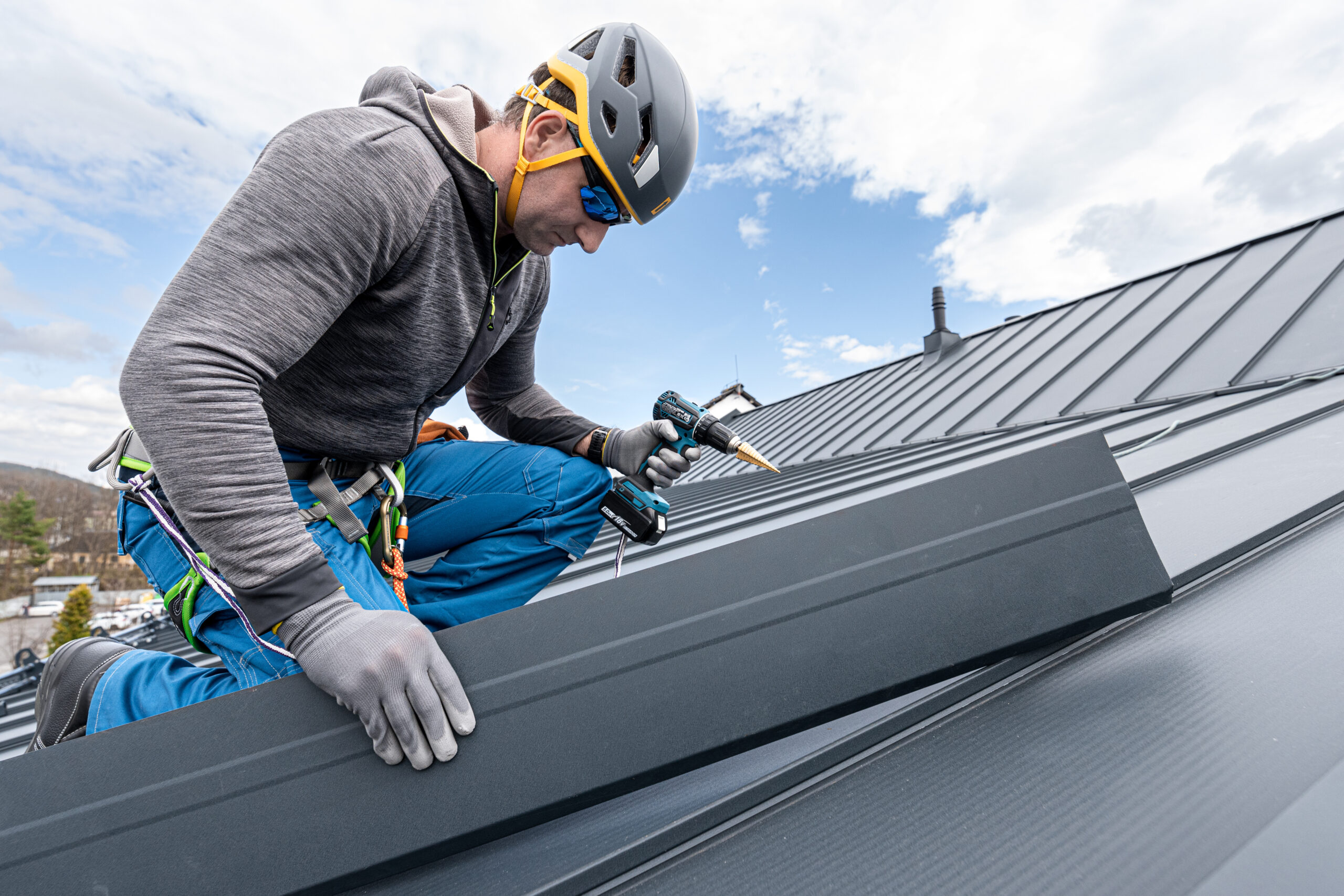 A roofer in safety gear repairing a metal roof