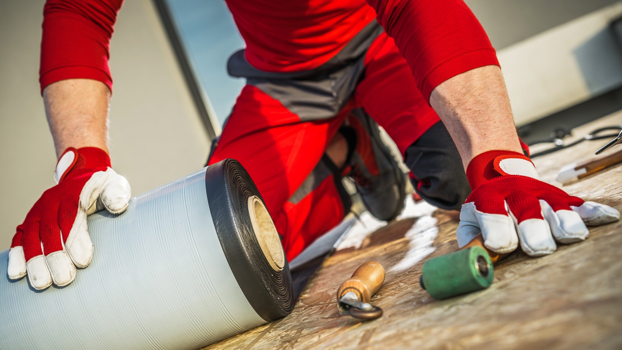 Roofer in red safety gear installing EPDM roofing on commercial roof