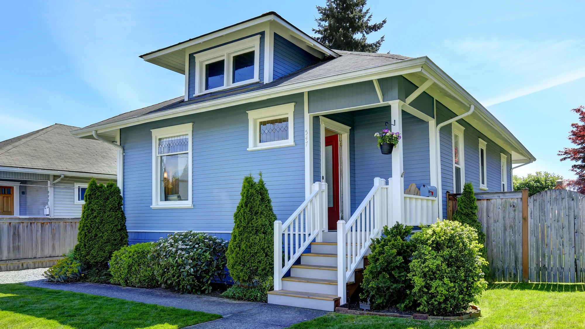 Exterior view of small home with bright blue siding, windows, and beautifully kept landscaping