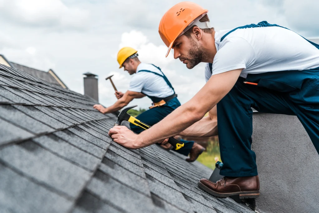 Roofers hammering nails in shingles on an asphalt shingle roof